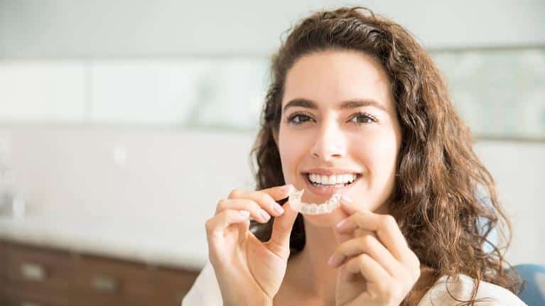 Patient holding tray of Invisalign at dentist near me Norfolk, MA